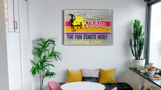 Image of a wooden sign hung up in a home as decor. The sign is an image of three surfers holding surfboards in front of a sunset on a beach, that says the fun starts here crystal cove.